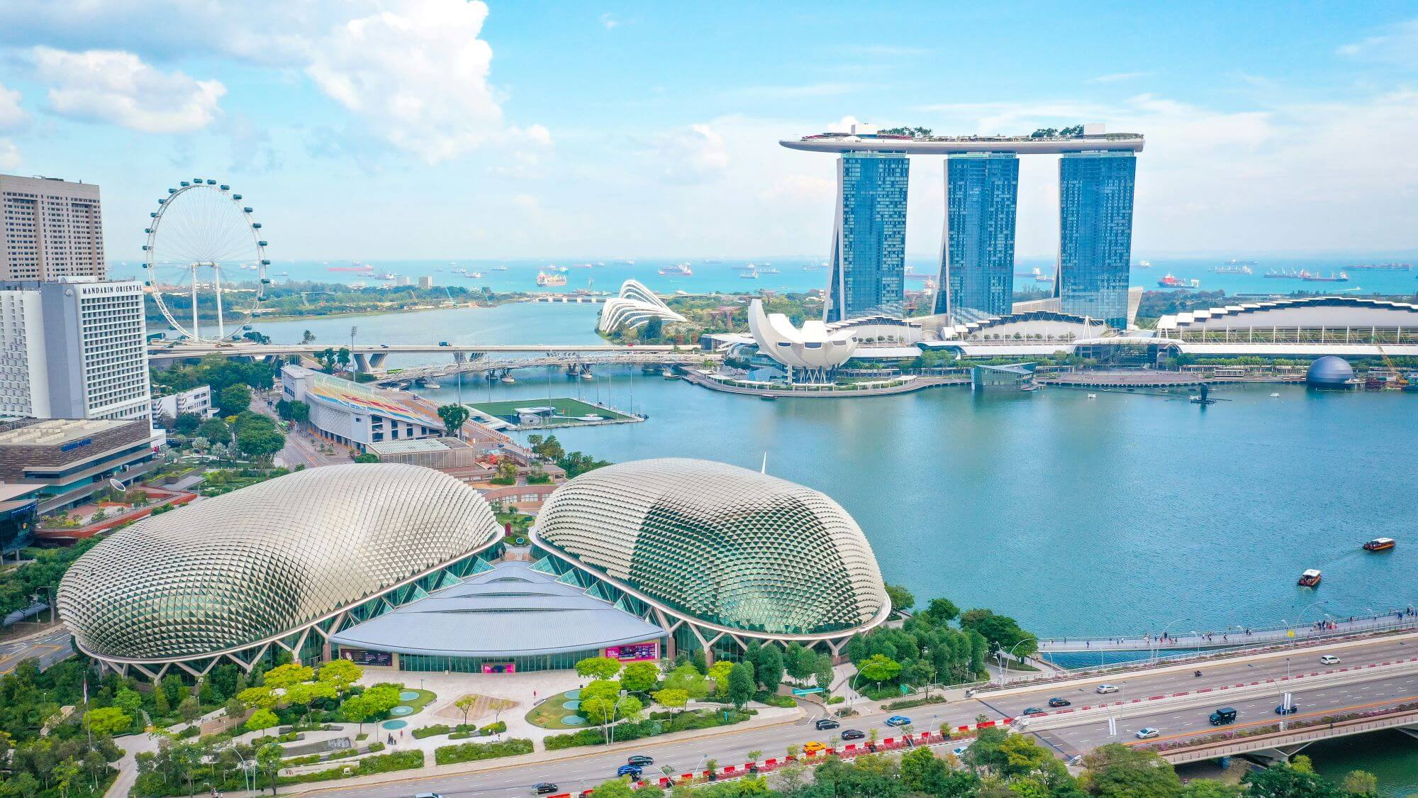 A panoramic view of singapore skyline featuring iconic architecture including marina bay sands and the artscience museum, with the singapore flyer ferris wheel in the distance, set against a backdrop of blue skies.