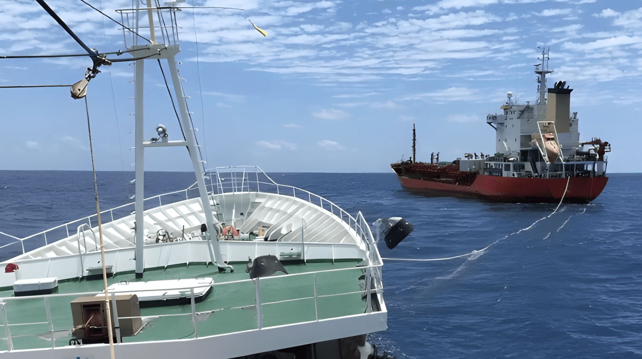 A view from the bow of a white ship, looking out at a red cargo vessel sailing across the deep blue ocean under a clear sky, showcasing innovative fuel solutions.