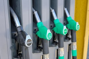 Four fuel pump handles at a gas station: one labeled Diesel, one E10, and two labeled Super Plus, all with green or black handles and hoses attached to a grey fuel dispenser.