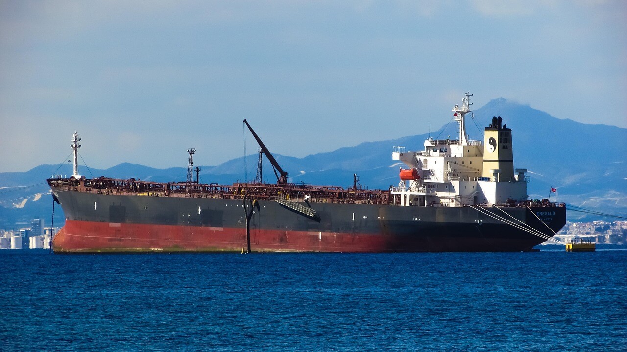 A large black and red oil tanker anchored in the sea with mountains in the background.